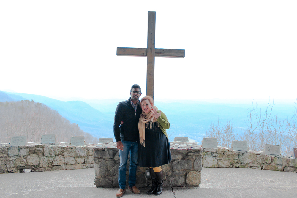 Couple Standing in front of the Cross at the Mountain Top.