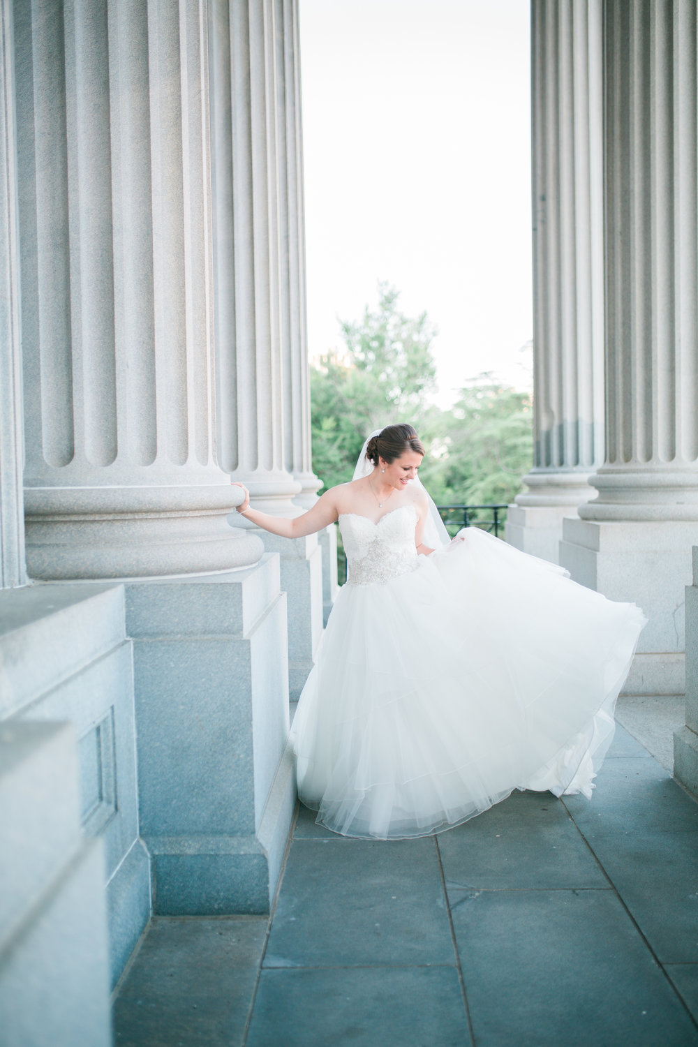 Bride holding dress and leaning hand on column